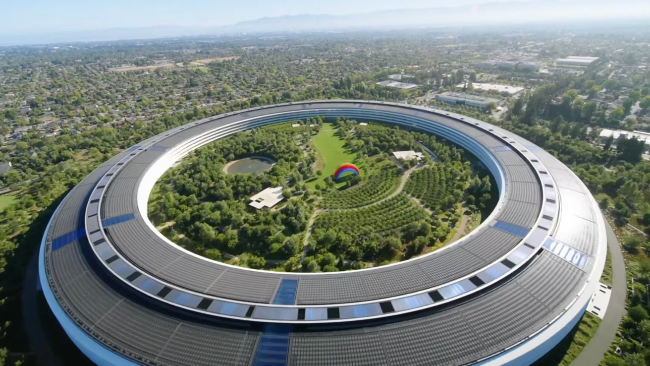 Circular building with solar panels, encircling lush greenery and trees, features a pond and colorful rainbow structure at the center, set in an expansive urban landscape.