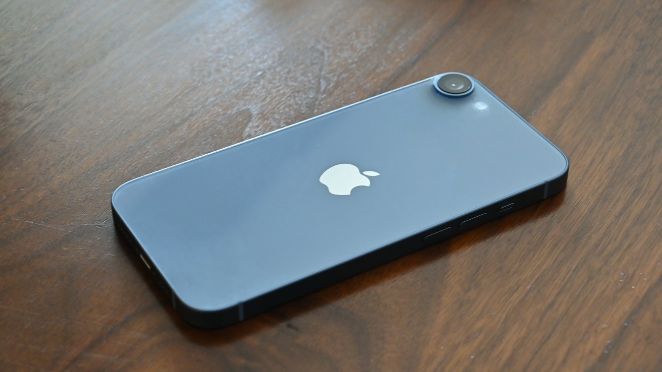 Smartphone with a blue back, single camera, and silver apple logo on a wooden surface.