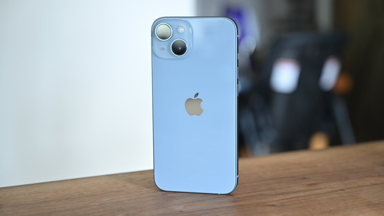 A light blue smartphone with dual cameras on a wooden surface, showing an apple logo.