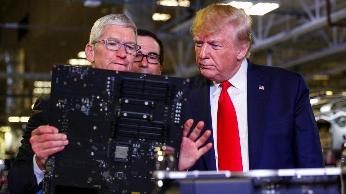 Three men closely examine a large circuit board in an industrial setting, one wearing glasses, another in a suit with a red tie.