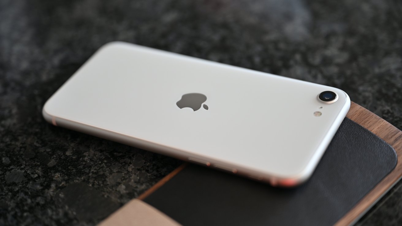 Silver iPhone SE with Apple logo lies on a dark textured surface, showcasing rear camera and sleek design.